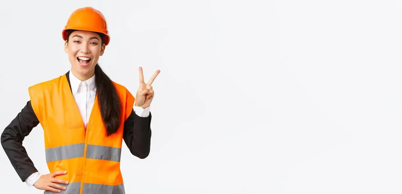 Cheerful, upbeat Asian female architect wearing a safety helmet and reflective jacket, giving a peace sign.